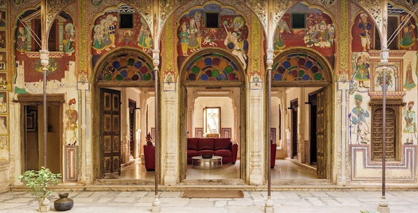 Un salón ornamentado con murales intrincados, un sofá rojo central y piso de piedra.