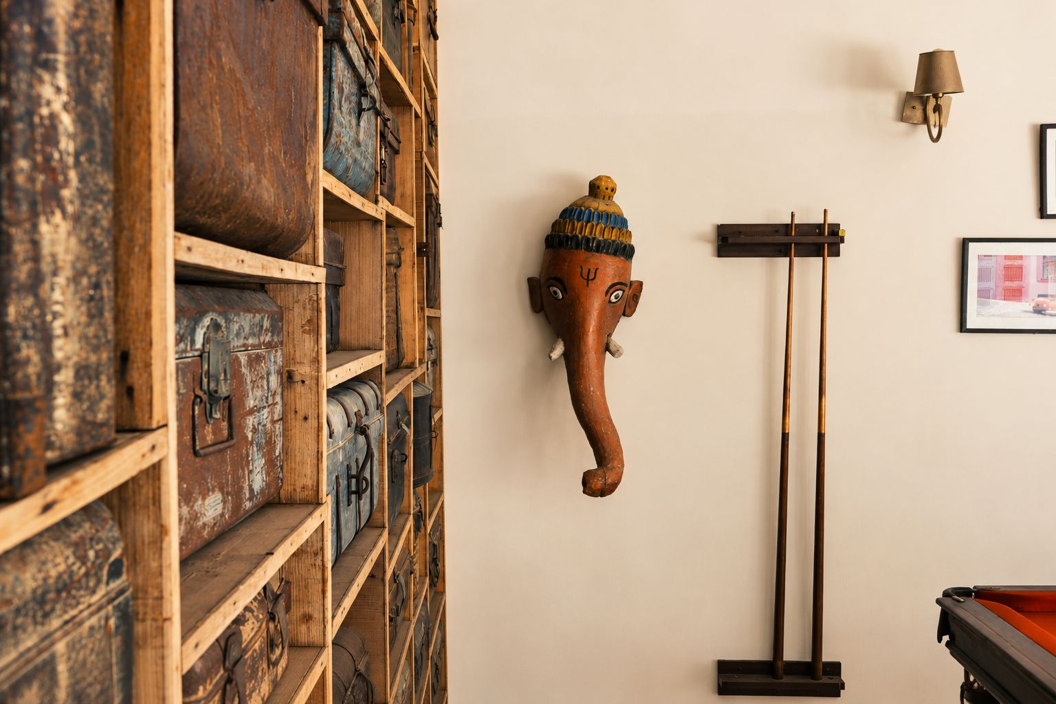 Una habitación con un mueble de madera lleno de varios recipientes, una escultura de cabeza de elefante en la pared, una lámpara de pared y un cuadro enmarcado.