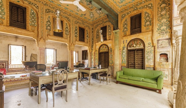 A room with ornate walls, a green sofa, a desk, and a chair. - Vivaana Culture Hotel (Churi Ajitgarh)