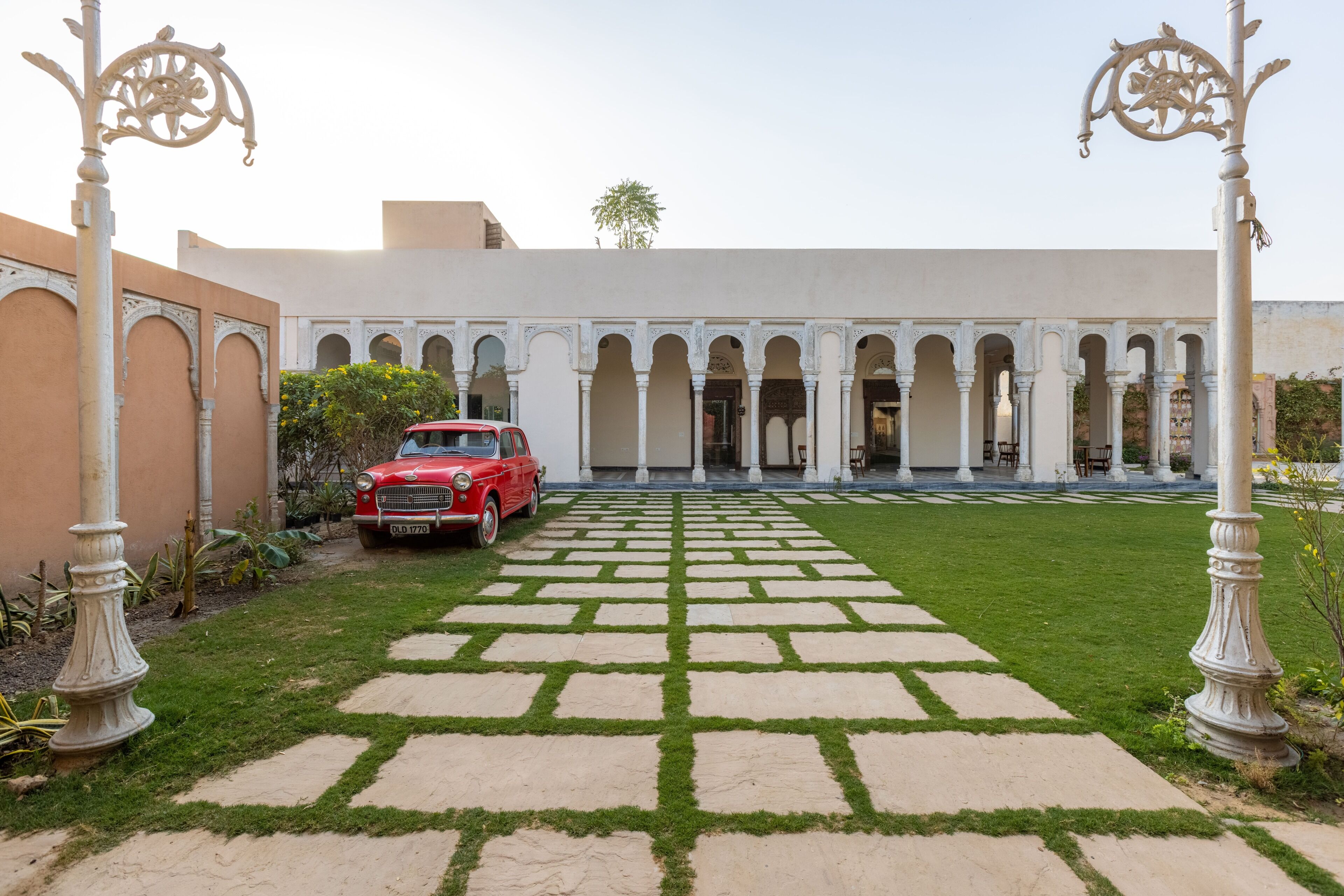 Un patio con un coche rojo estacionado frente, rodeado de columnas y arcos blancos.