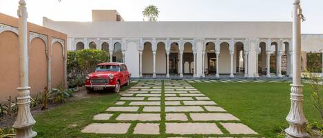 Un patio con un coche rojo estacionado frente, rodeado de columnas y arcos blancos.