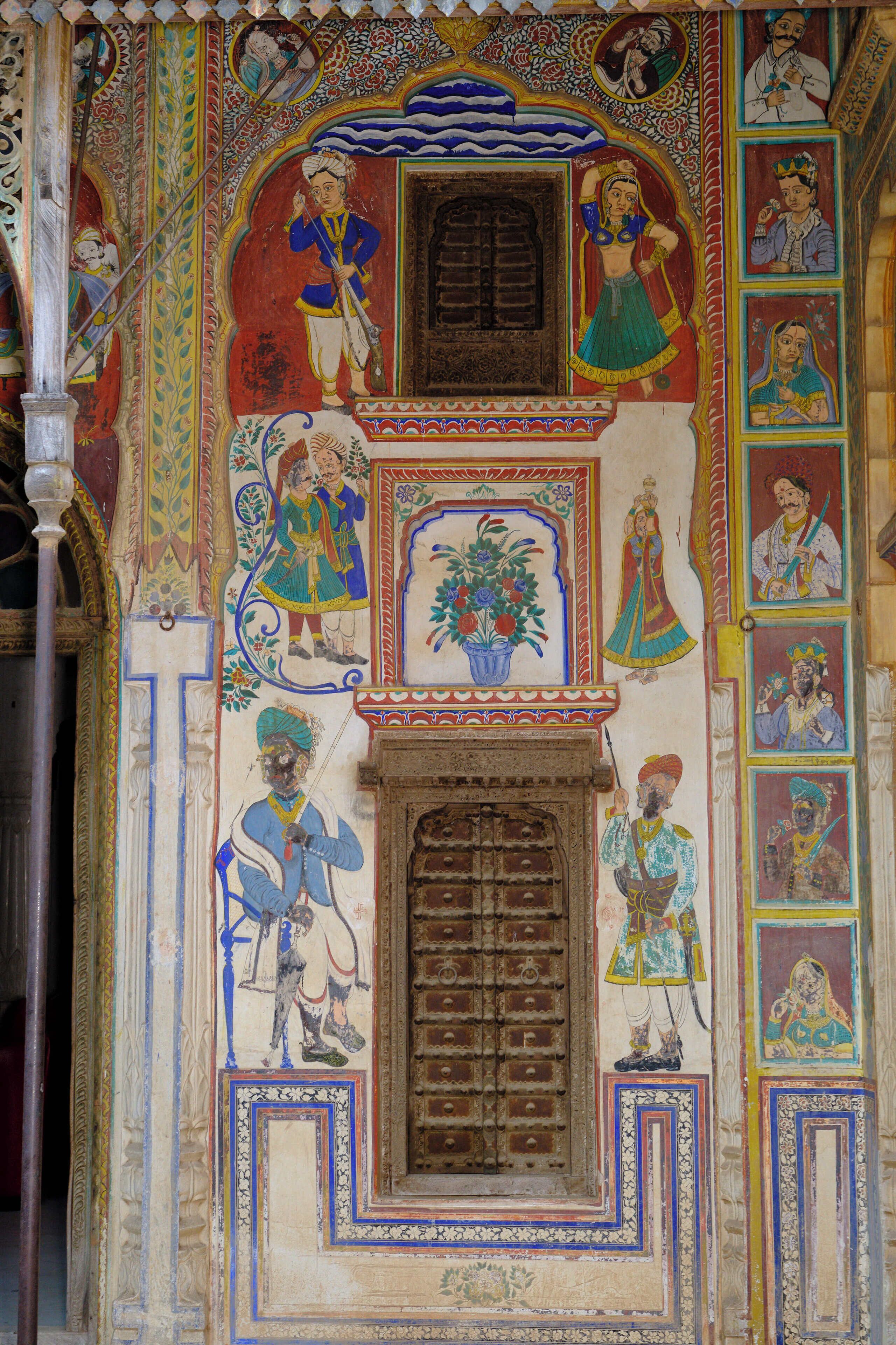 A wall with intricate traditional artwork, including figures and floral patterns.