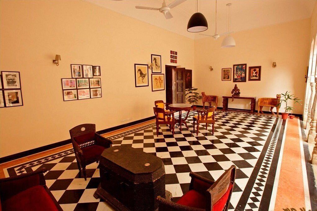 A hotel lobby with a checkered floor, a dining area with chairs and a table, and framed pictures on the walls.