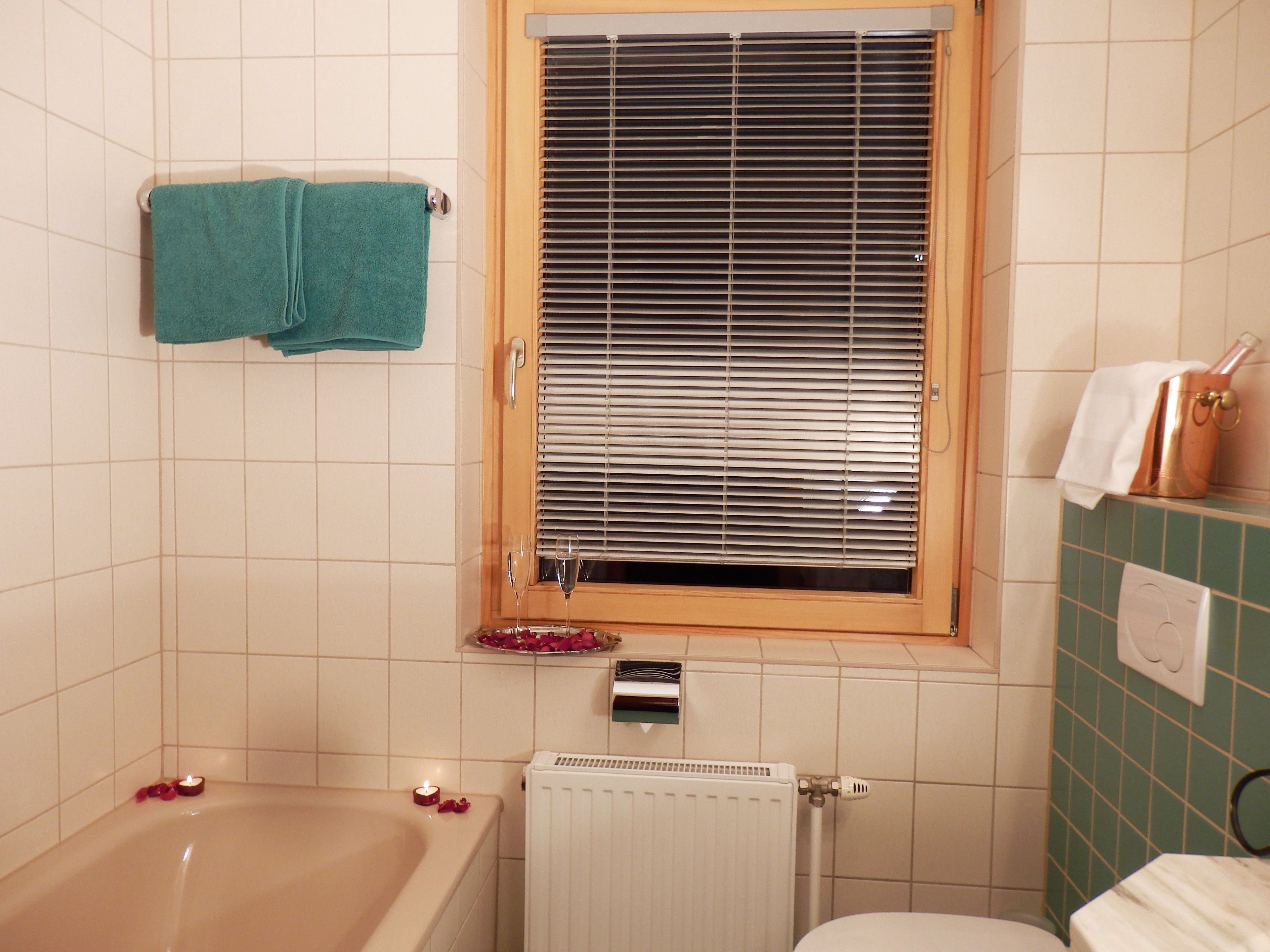 Un baño con bañera, una ventana con persianas, un perchero, un radiador y un inodoro.