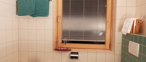 Un baño con bañera, una ventana con persianas, un perchero, un radiador y un inodoro.