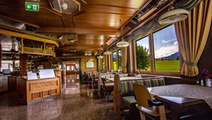 Un restaurante con cabinas y mesas de madera, una zona de bar y amplios ventanales con vistas al exterior.