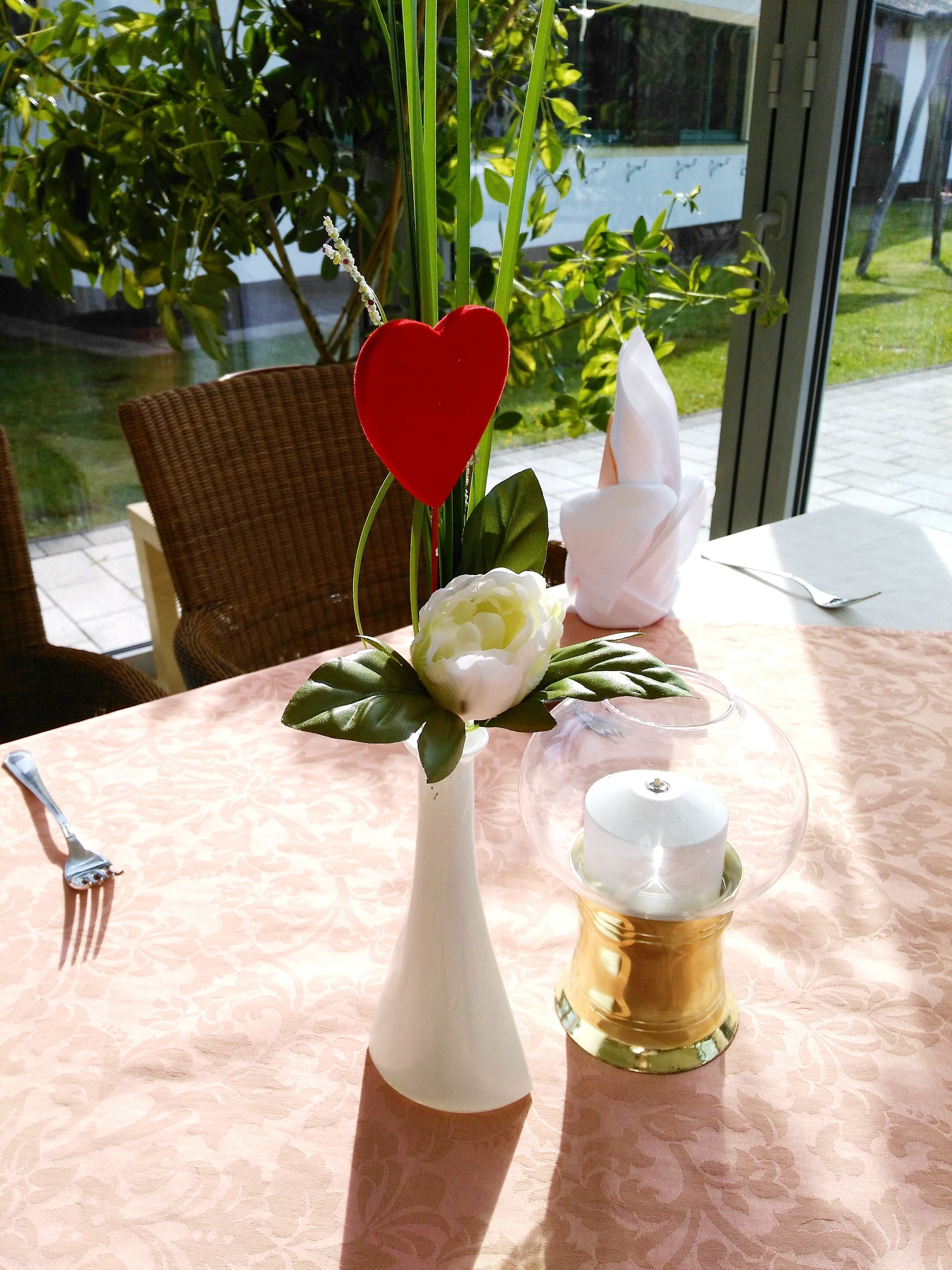 Una mesa con un jarrón blanco, una campana de cristal y un arreglo floral blanco.