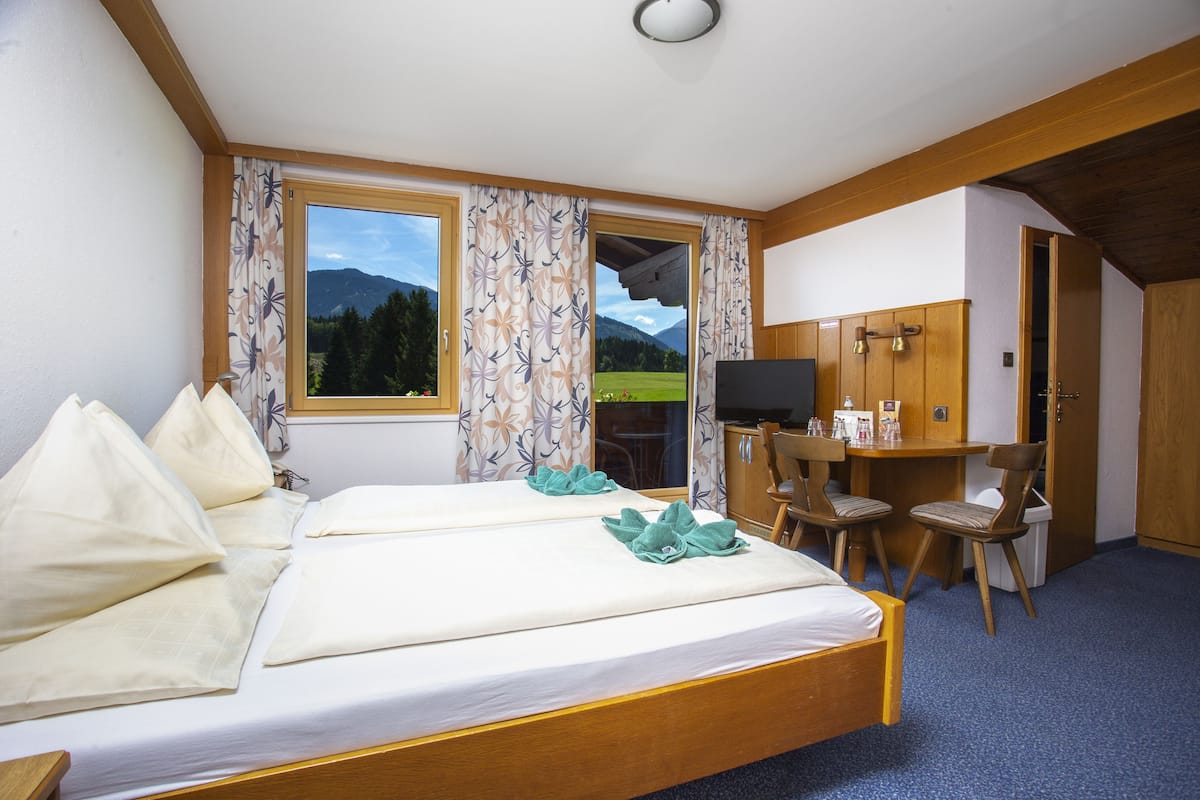 Quarto de hotel com duas camas, uma mesa de trabalho e televisão, e vista para as montanhas pela janela.