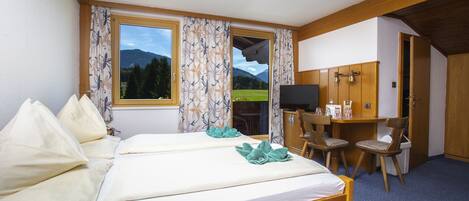 A hotel room with two beds, a desk with a TV, and a view of mountains through the window.