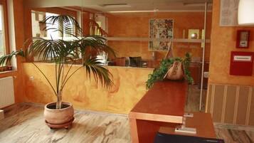 A reception area with a wooden reception desk, a large potted plant, and a wall with framed pictures.