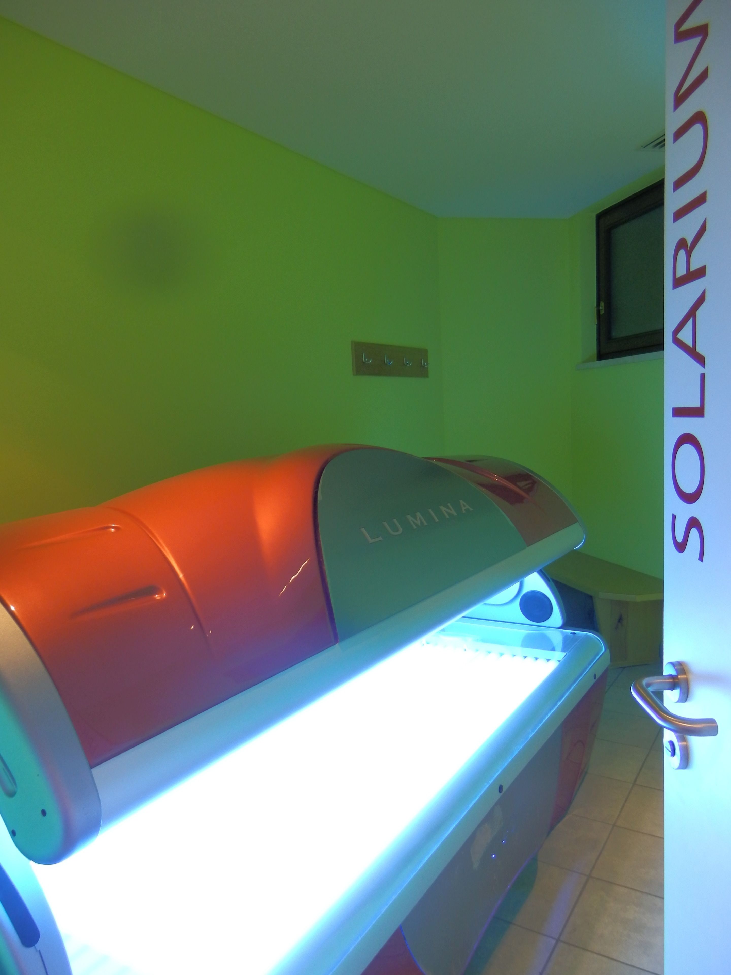 Ein Raum mit einem Massagesessel, der mit 'LUMINA' beschriftet ist, und einem Wandzeichen mit der Aufschrift 'SOLARIUM'.