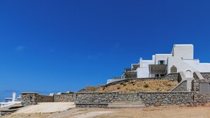 Un bâtiment blanc aux murs de pierre, avec des marches menant à l’entrée, se dressant sur un fond de ciel bleu clair.