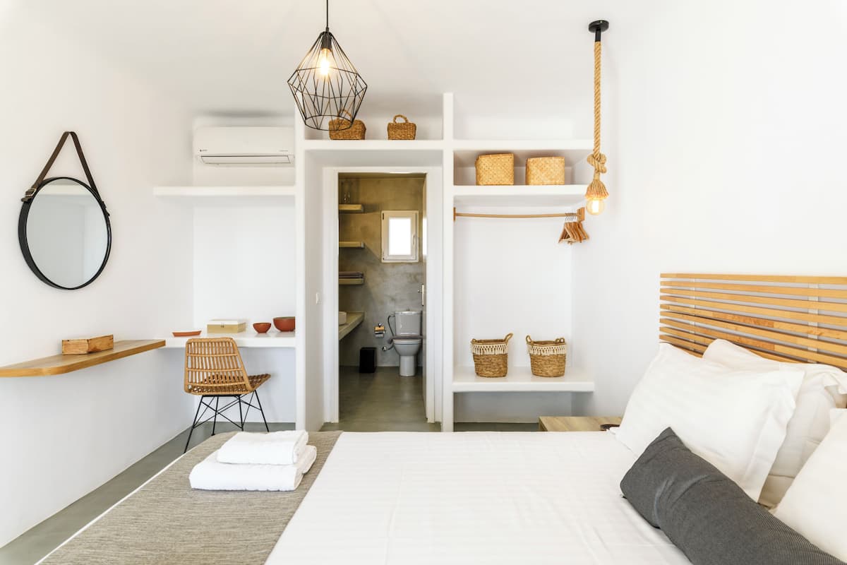Una camera da letto con un letto, una sedia, uno scaffale con cesti, una lampada a sospensione e un condizionatore d'aria.
