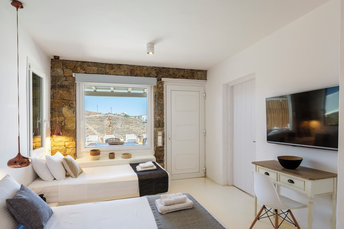 Una camera da letto moderna con una parete in pietra, una grande finestra, un letto, una televisione e un piccolo tavolino.