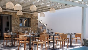 Un espace de restauration en plein air avec des chaises et des tables en osier, un mur en pierre et des lampes en osier suspendues.