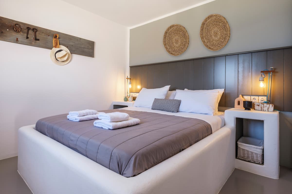 Un letto rifatto con asciugamani piegati, una testiera con luci a parete e un comodino con una lampada e un cesto.