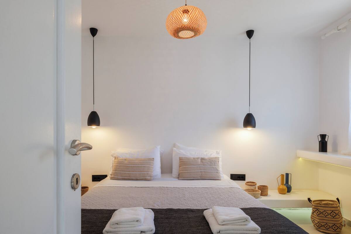Un letto rifatto con due cuscini, un comodino con una lampada e un lampadario a sospensione sopra.