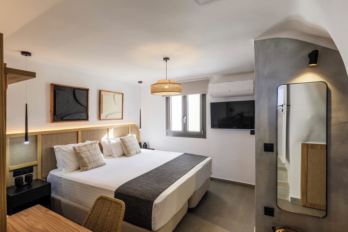 Una camera d'albergo moderna con un letto grande, una scrivania, una sedia, una lampada a sospensione e uno specchio fissato al muro.