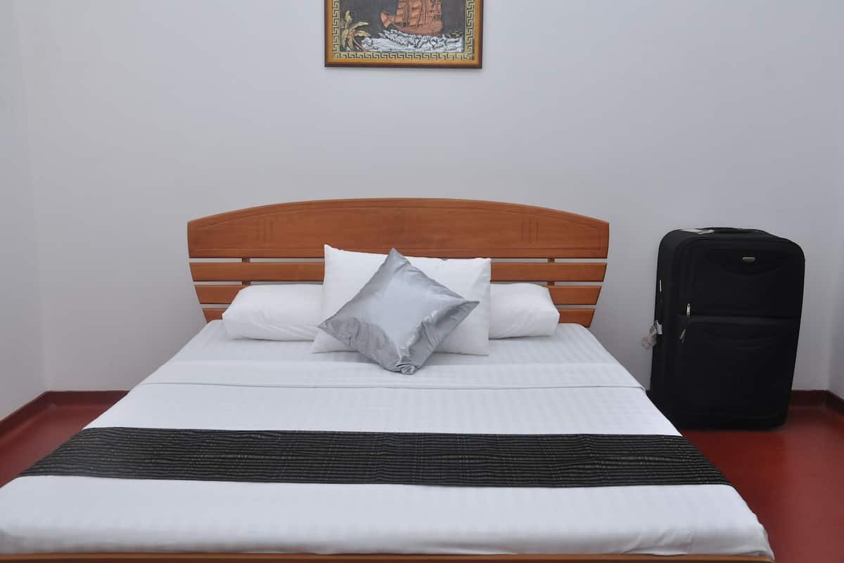 A neatly made bed with white bedding and a grey pillow, a black suitcase on the floor, and a framed picture on the wall.