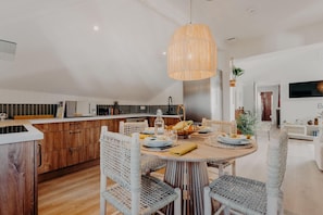 Une cuisine moderne avec un coin repas, comprenant une table ronde en bois, des chaises en osier et un luminaire suspendu.
