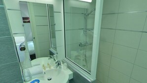 A modern bathroom with a glass shower enclosure, a sink with a mirror, and a towel rack. - Hotel Palym (Biarritz)