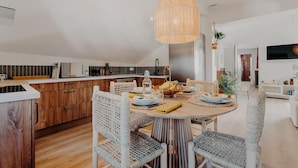 Uma cozinha moderna com área de jantar, apresentando uma mesa redonda de madeira, cadeiras de vime e um lustre.