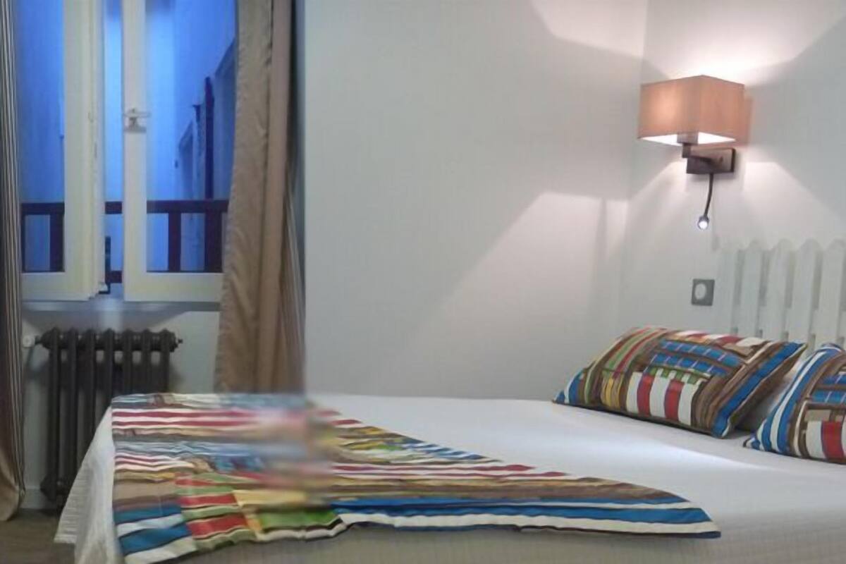 A hotel room with a bed, a chair, a window with curtains, and two wall-mounted lamps.