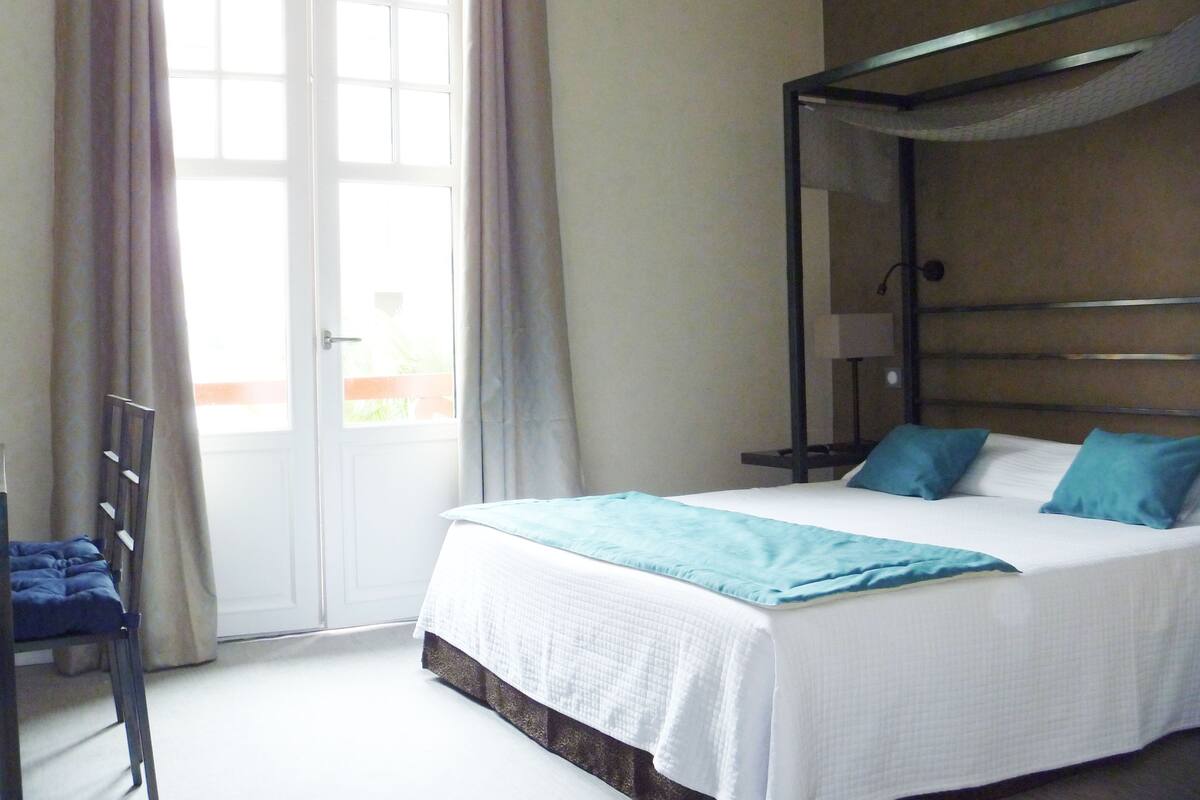 A hotel room with a bed, a window with curtains, a bedside table, and a chair.