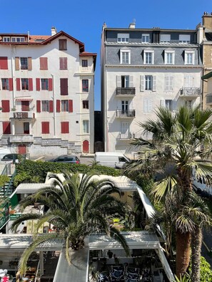 Un immeuble à plusieurs étages doté de balcons, avec un rez-de-chaussée visible où se trouve un magasin, et entouré de palmiers.