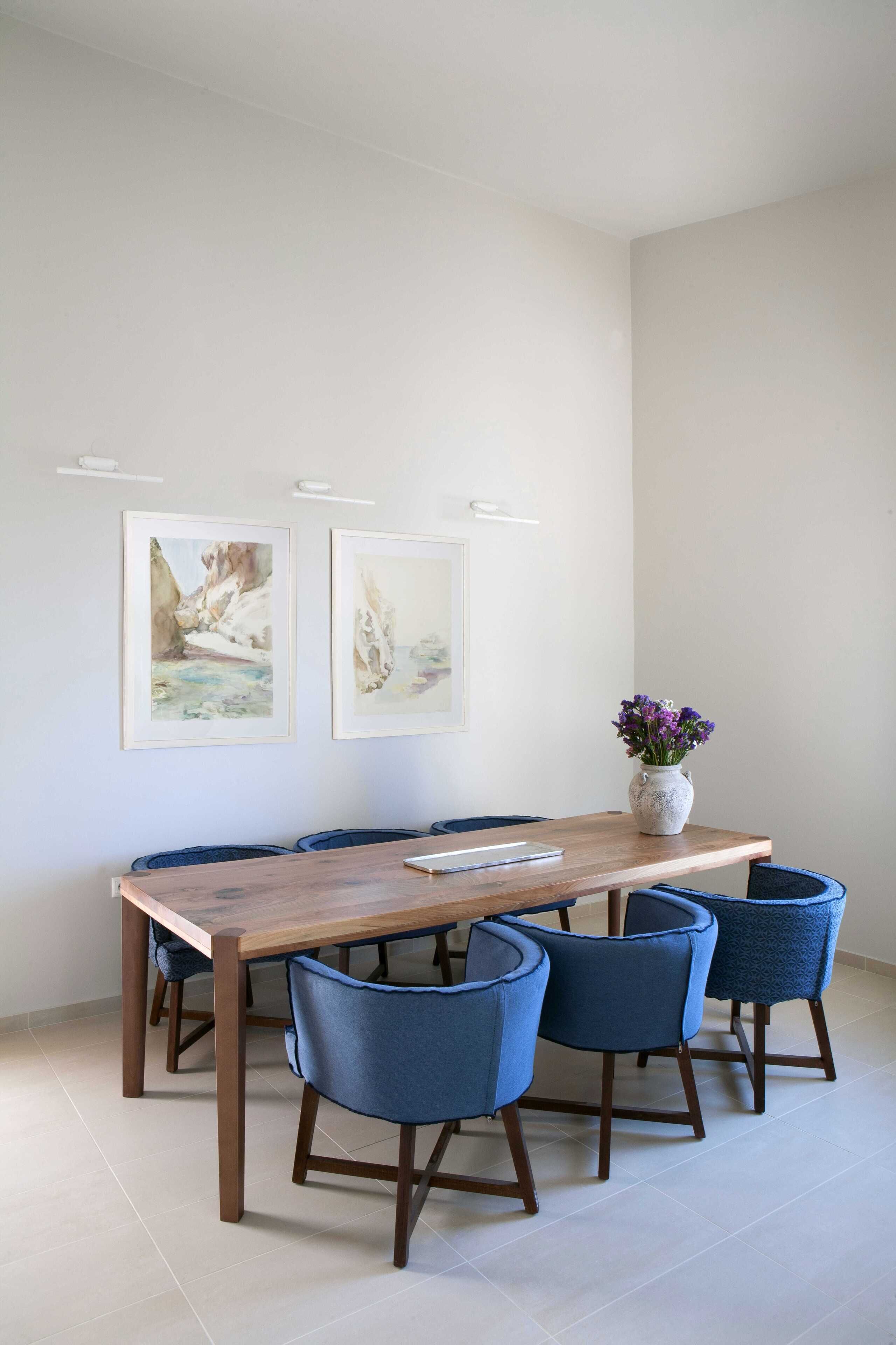 A dining area with a wooden table, six blue chairs, and two framed artworks on the wall.
