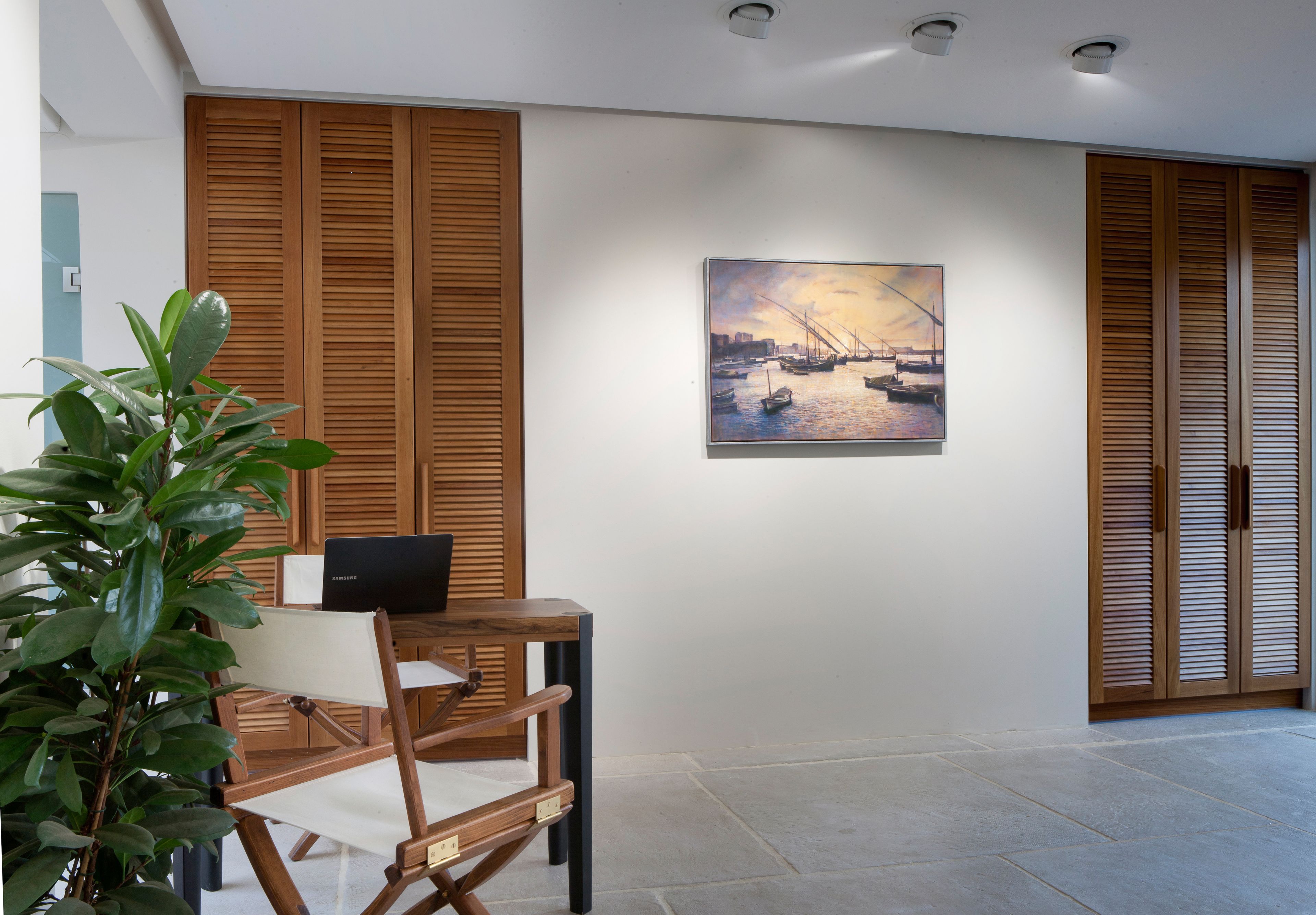 A modern interior with a wooden desk, a laptop, and a painting of a harbor scene.