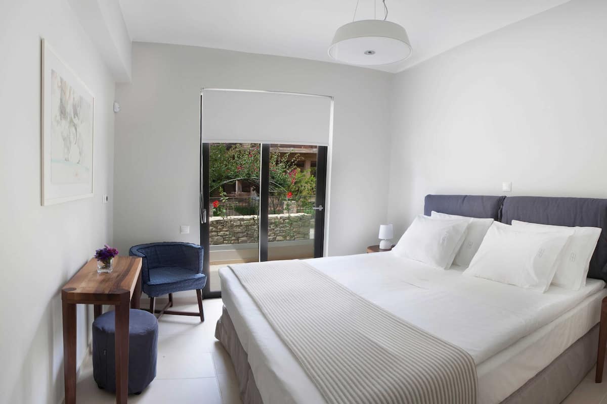 Un dormitorio con cama, escritorio, silla, lámpara y vistas a un jardín a través de una puerta corredera.