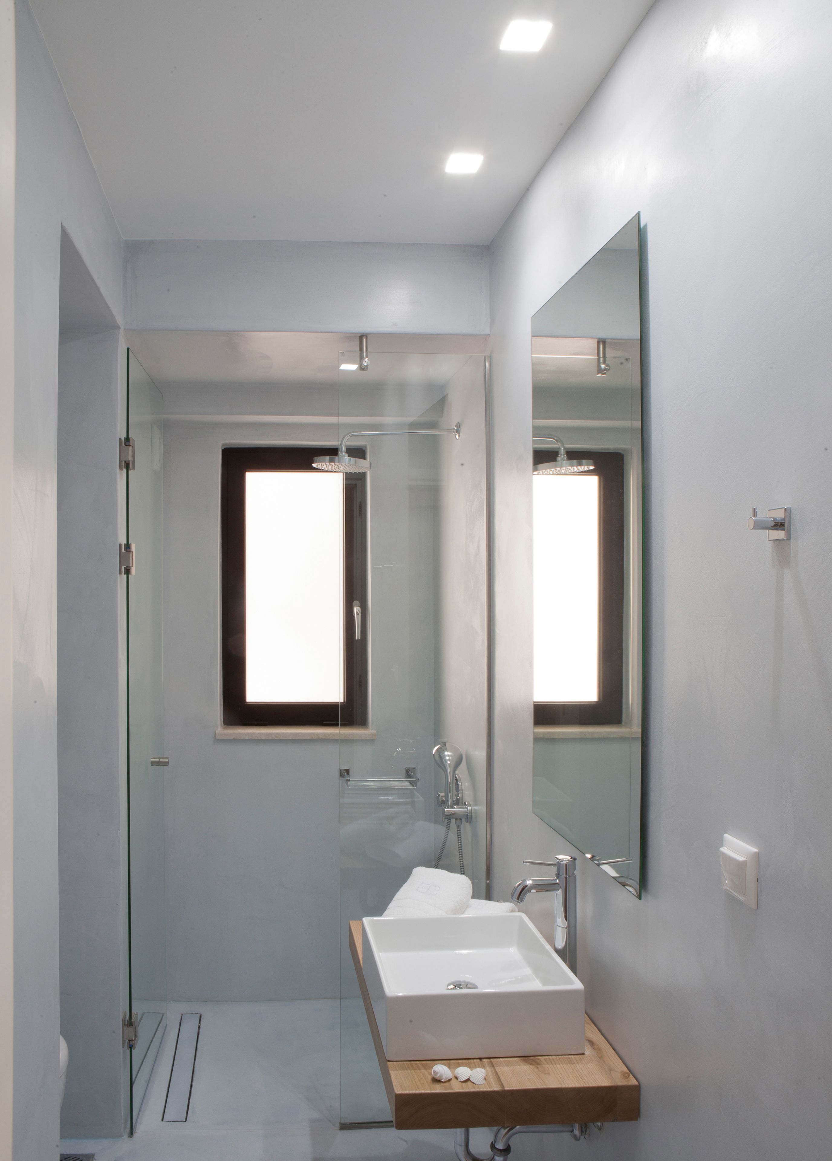 Un baño moderno con cabina de ducha de vidrio, un lavabo blanco con encimera de madera y un espejo grande.
