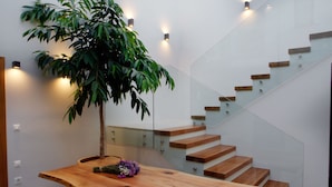 A modern interior with a wooden table, a potted plant, and a glass staircase. - Aethrion Homes (Chania)