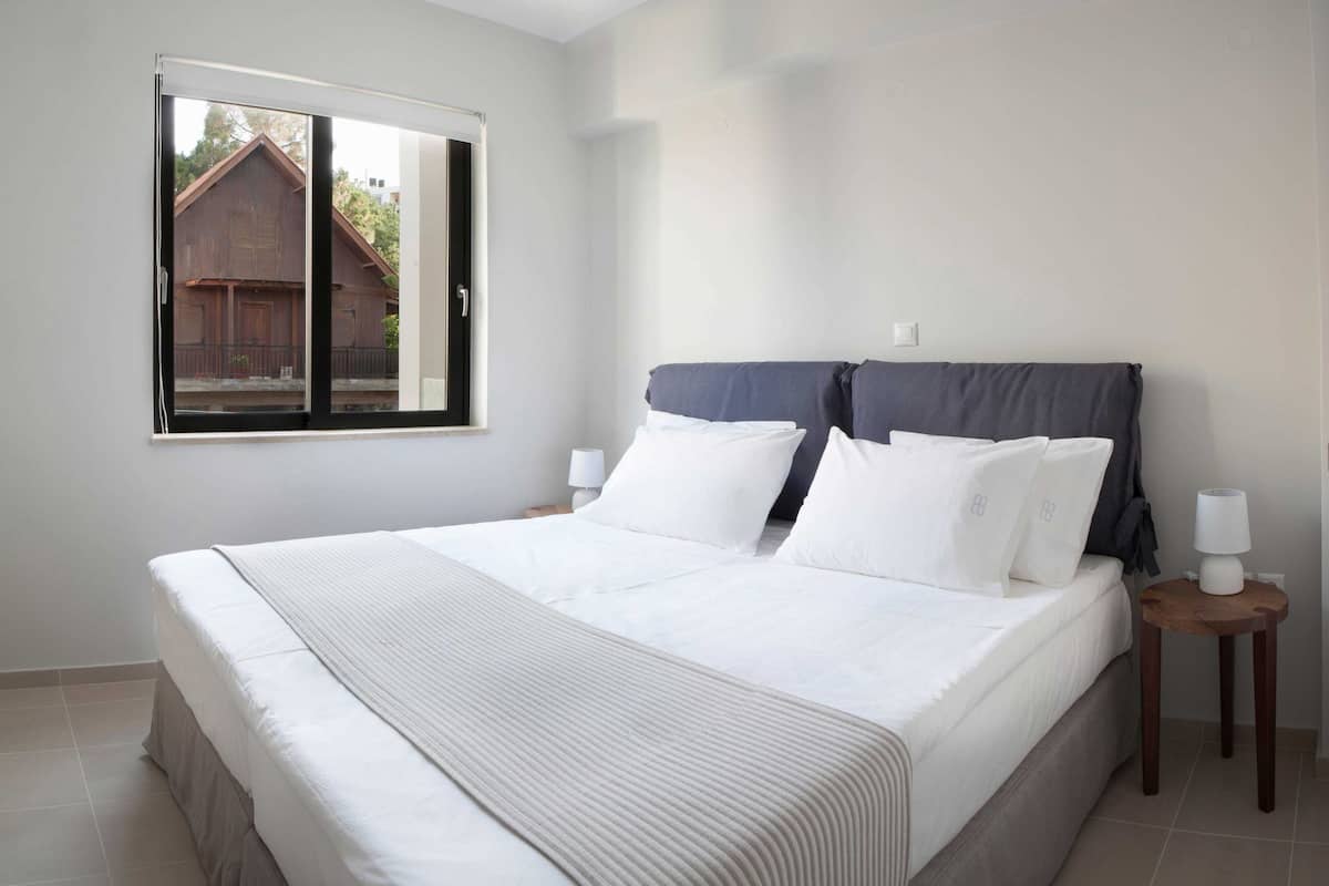 Un dormitorio con una cama grande, una ventana y una mesita de noche con lámpara.