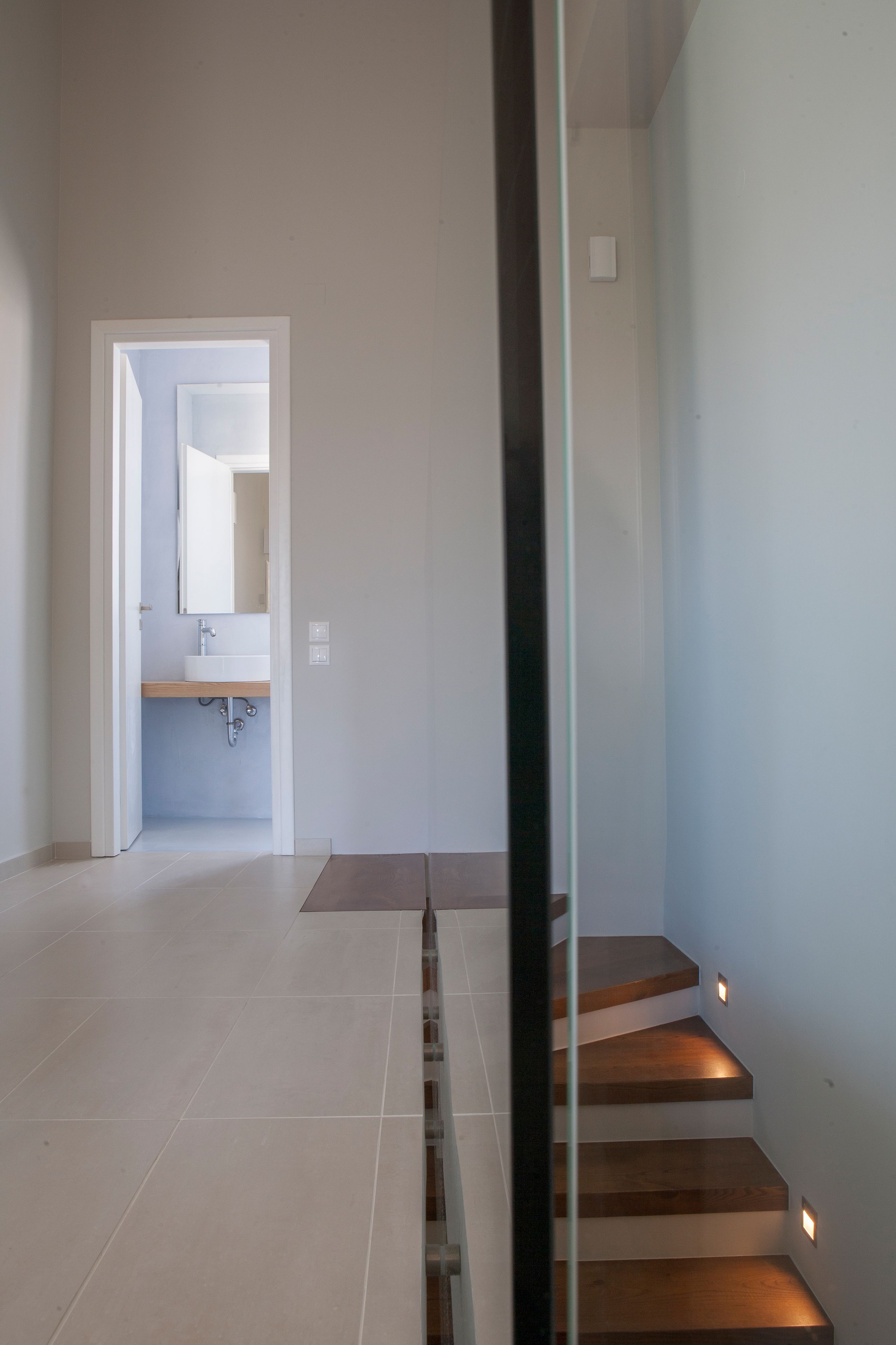 A modern interior with a staircase leading to a second floor, a visible bathroom with a sink and mirror, and a clean, minimalist design.