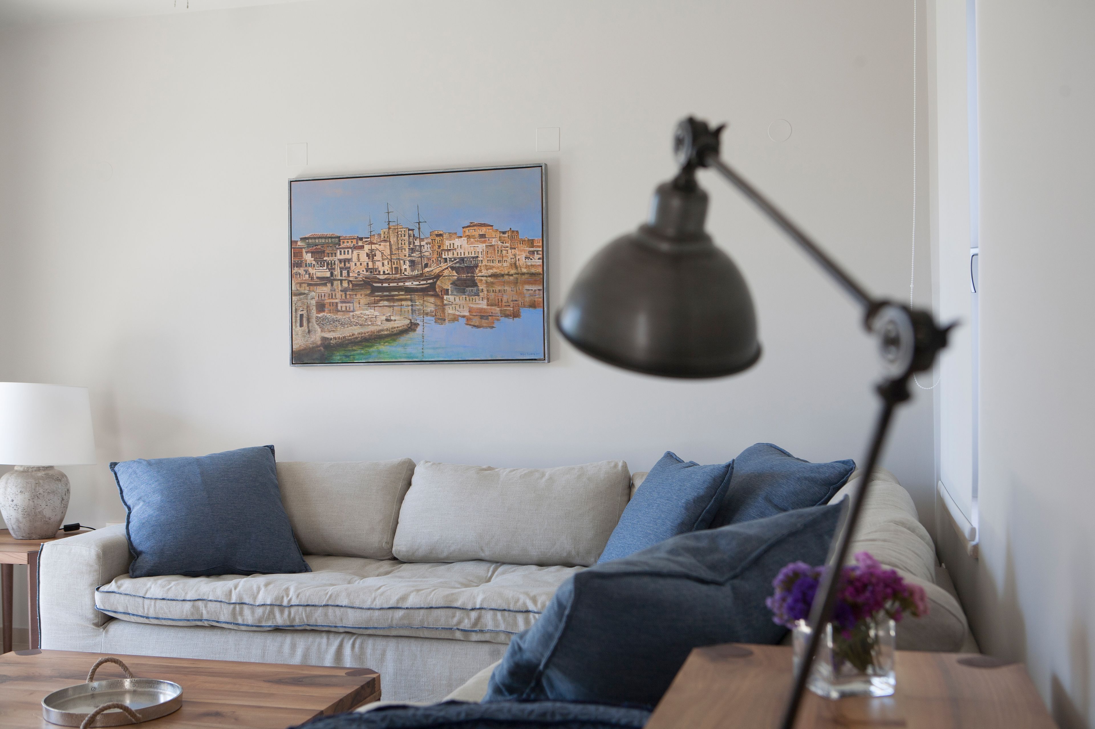 A living room with a sofa, a lamp, a painting, and a vase with flowers.