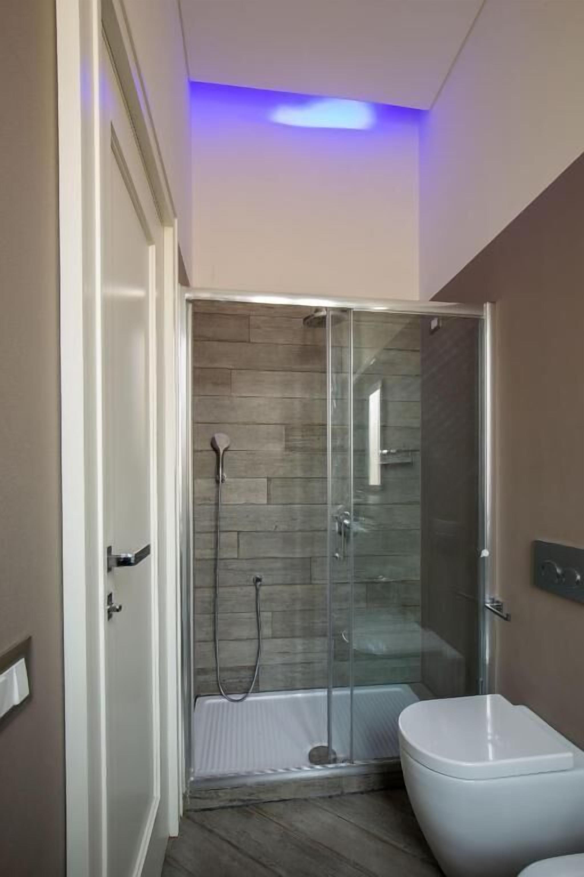 Un baño moderno con ducha envuelta en cristal, inodoro blanco y suelo de madera.