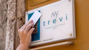Una mano insertando una tarjeta en una ranura de un cartel anunciando 'trevi Charming & Luxury Rooms Rome'.