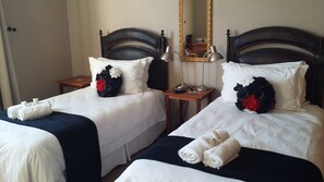Two twin beds with white linens and dark headboards, each with a decorative pillow and a small table beside.