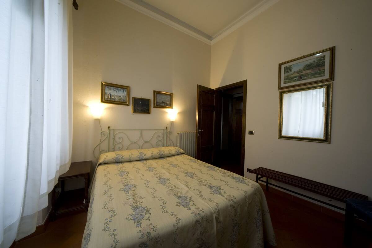 Una camera da letto con un letto, una panca di legno, un termosifone e tre quadri appesi al muro.