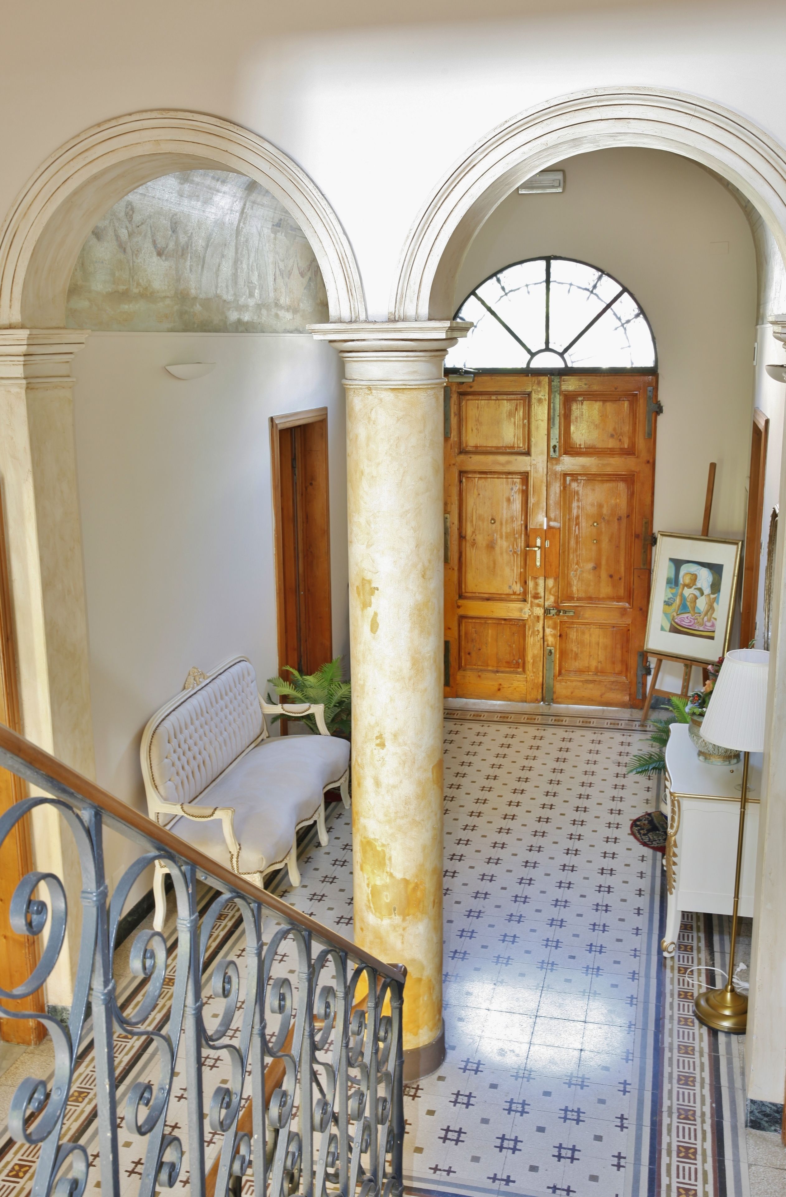 Um corredor com uma porta de madeira, um banco e um cavalete com uma pintura.