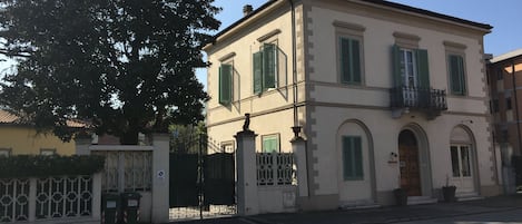 A two-story building with a symmetrical facade, green shutters, and a central entrance with a decorative gate.