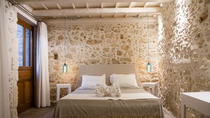 A stone-walled bedroom with a bed, two bedside tables, and a wooden door.