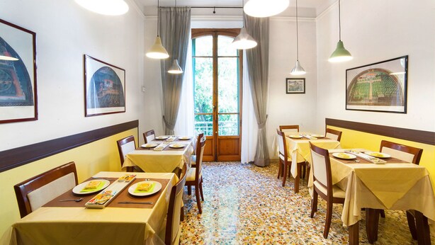 Un comedor con mesas dispuestas para comidas, cuadros en las paredes y vistas a través de una ventana.