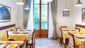 Un comedor con mesas dispuestas para comidas, un ventanal con cortinas y lámparas colgantes.
