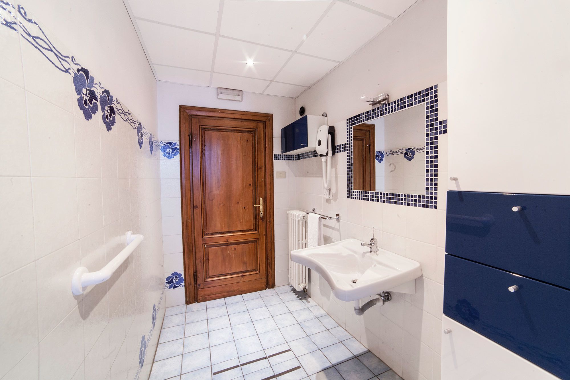 Ein Badezimmer mit Holztür, weißem Waschbecken und blautonierten Fliesen.