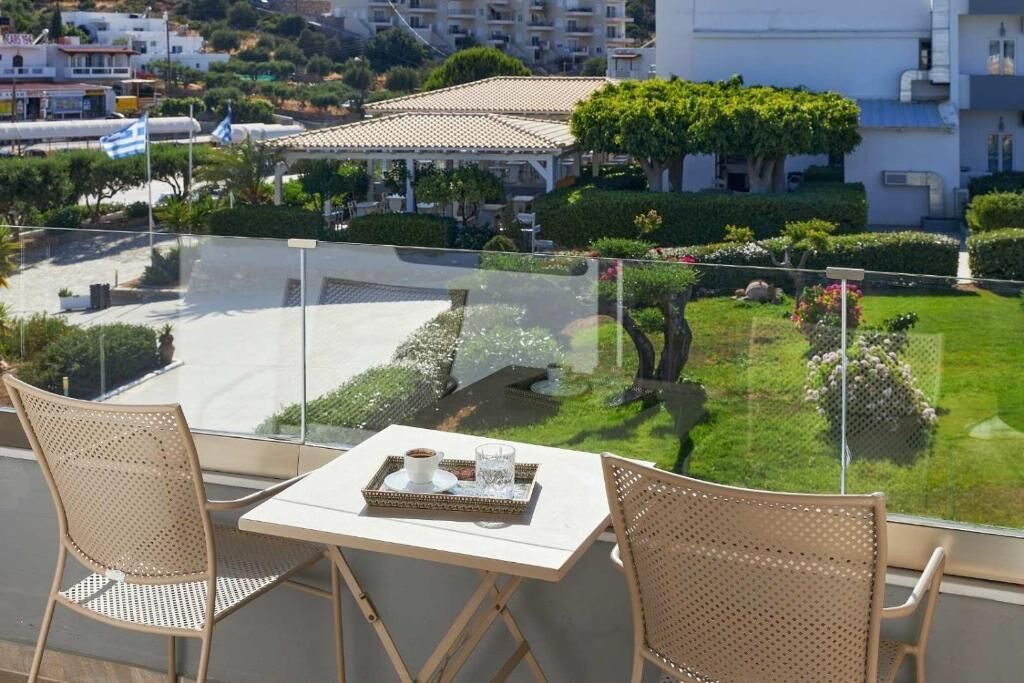 A balcony with two wicker chairs and a small table, overlooking a well-maintained garden and a residential area.