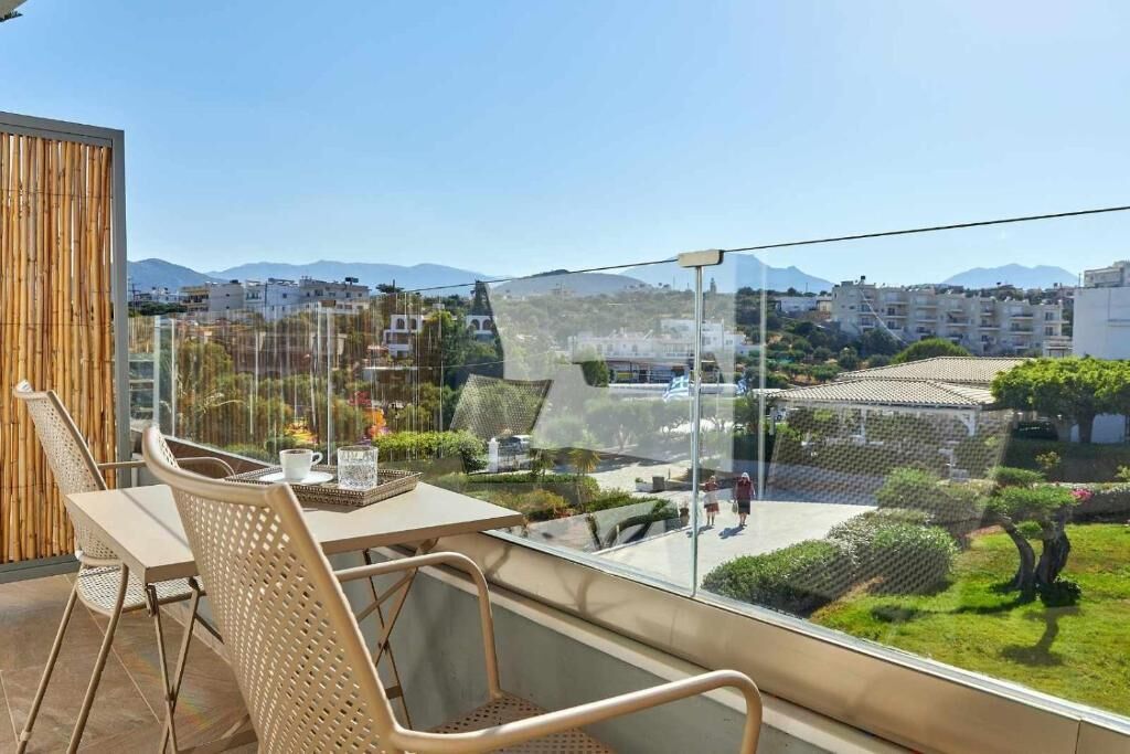 A balcony with a table and chairs, overlooking a residential area with houses and a mountain in the distance.