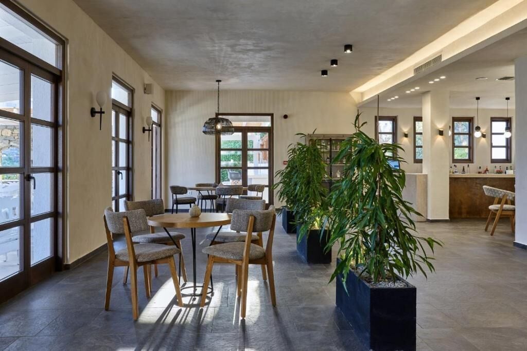 Un espace intérieur spacieux, doté de grandes fenêtres, de chaises en bois, d’une table ronde et de plantes en pot.